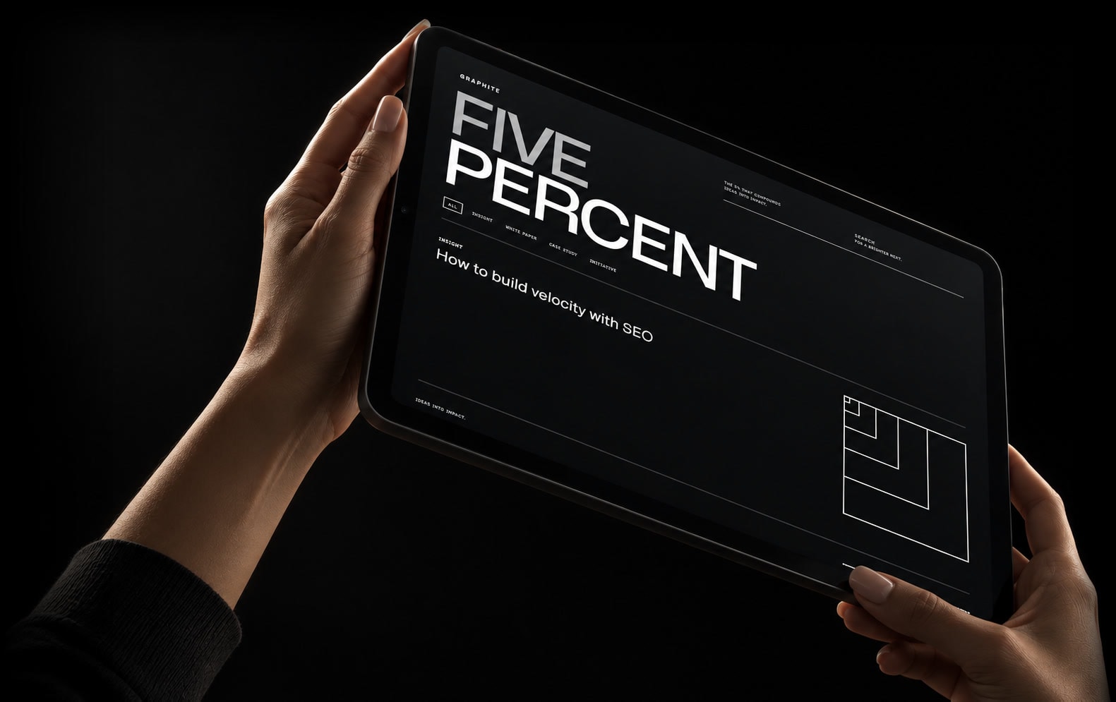 Hands holding a tablet displaying the Graphite Five Percent website against a dark background